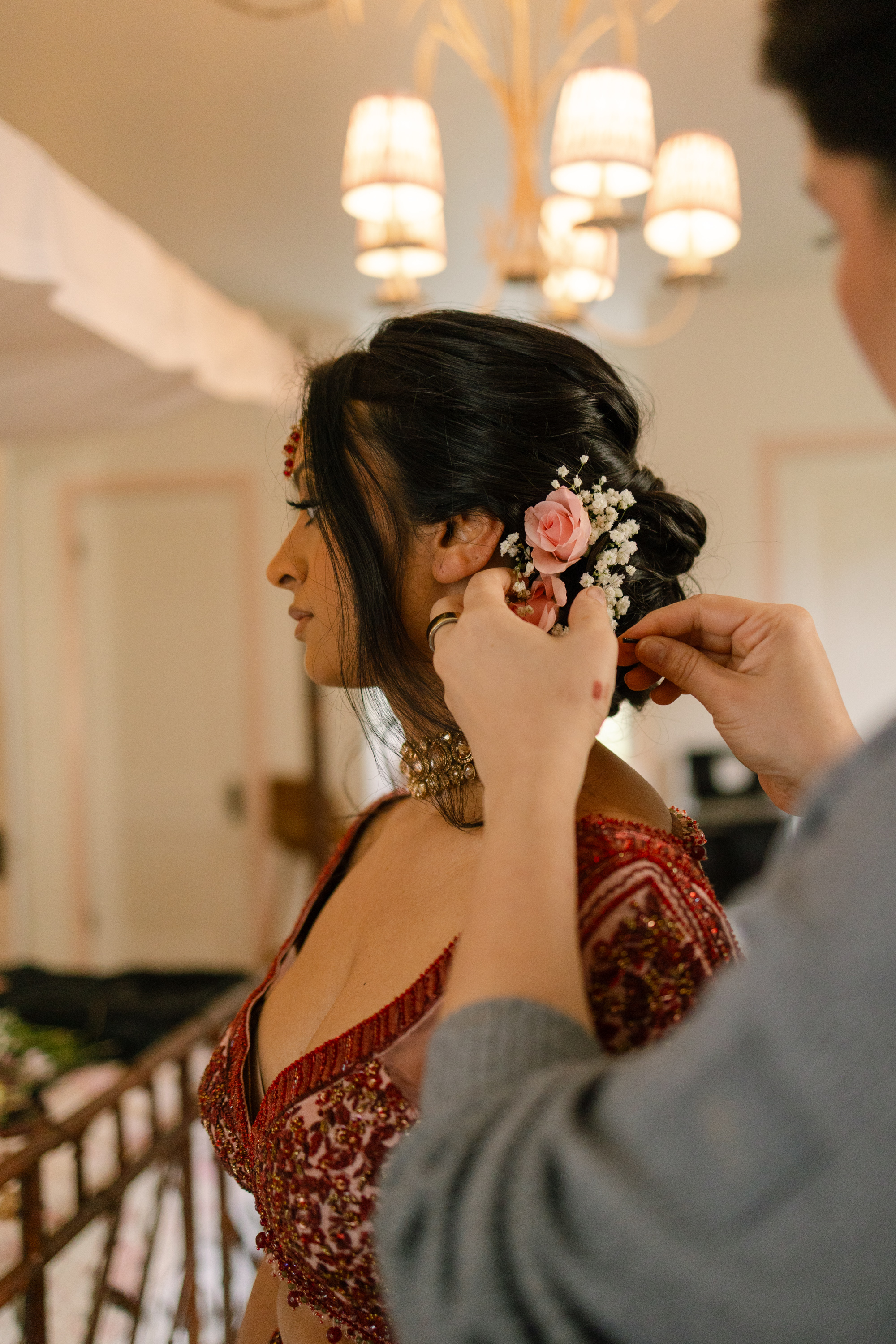 Hairstylist adding real pink roses and baby’s breath to a bride’s low wedding updo