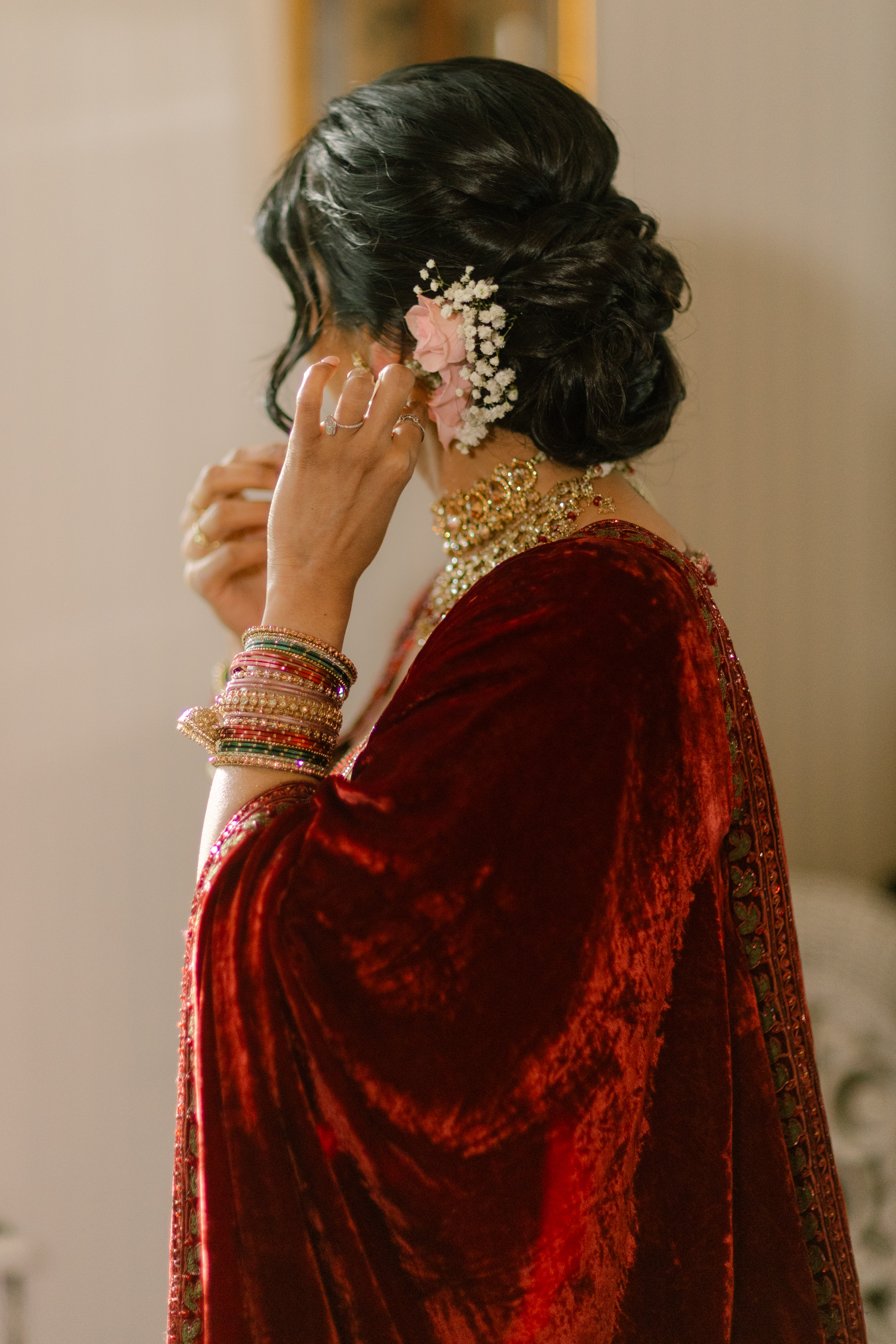 Bride wearing real pink roses and baby’s breath in a low bridal updo with red wedding outfit